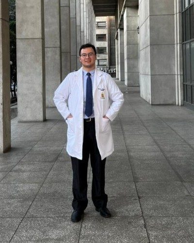 Mauricio Aguilera López, médico cirujano, con delantal blanco entre pilares de piedra